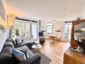 A modern living room with a sofa, a dining table with chairs, and large windows.