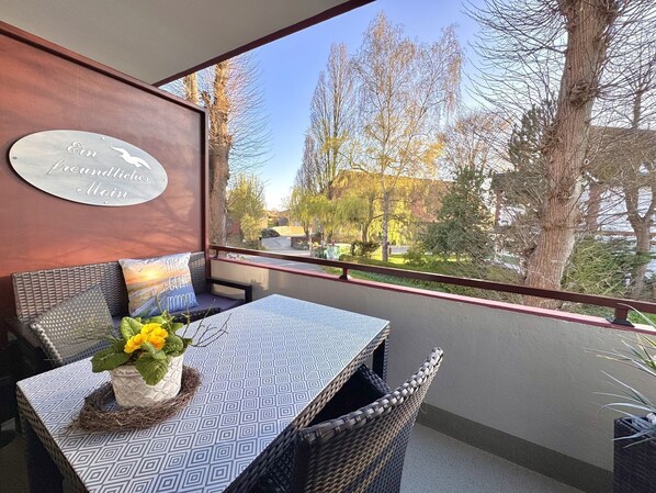 A balcony with wicker furniture, a table with a patterned tablecloth, and a view of trees and buildings.