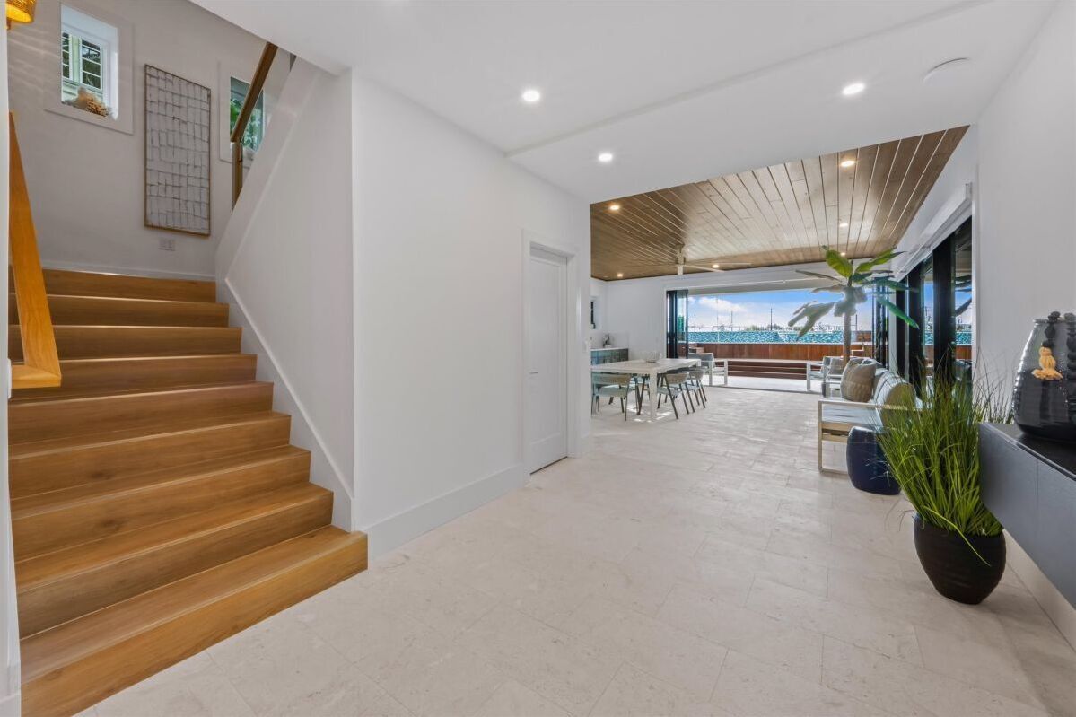Un intérieur moderne avec un escalier en bois, un coin repas et une vue dégagée grâce à de grandes fenêtres.