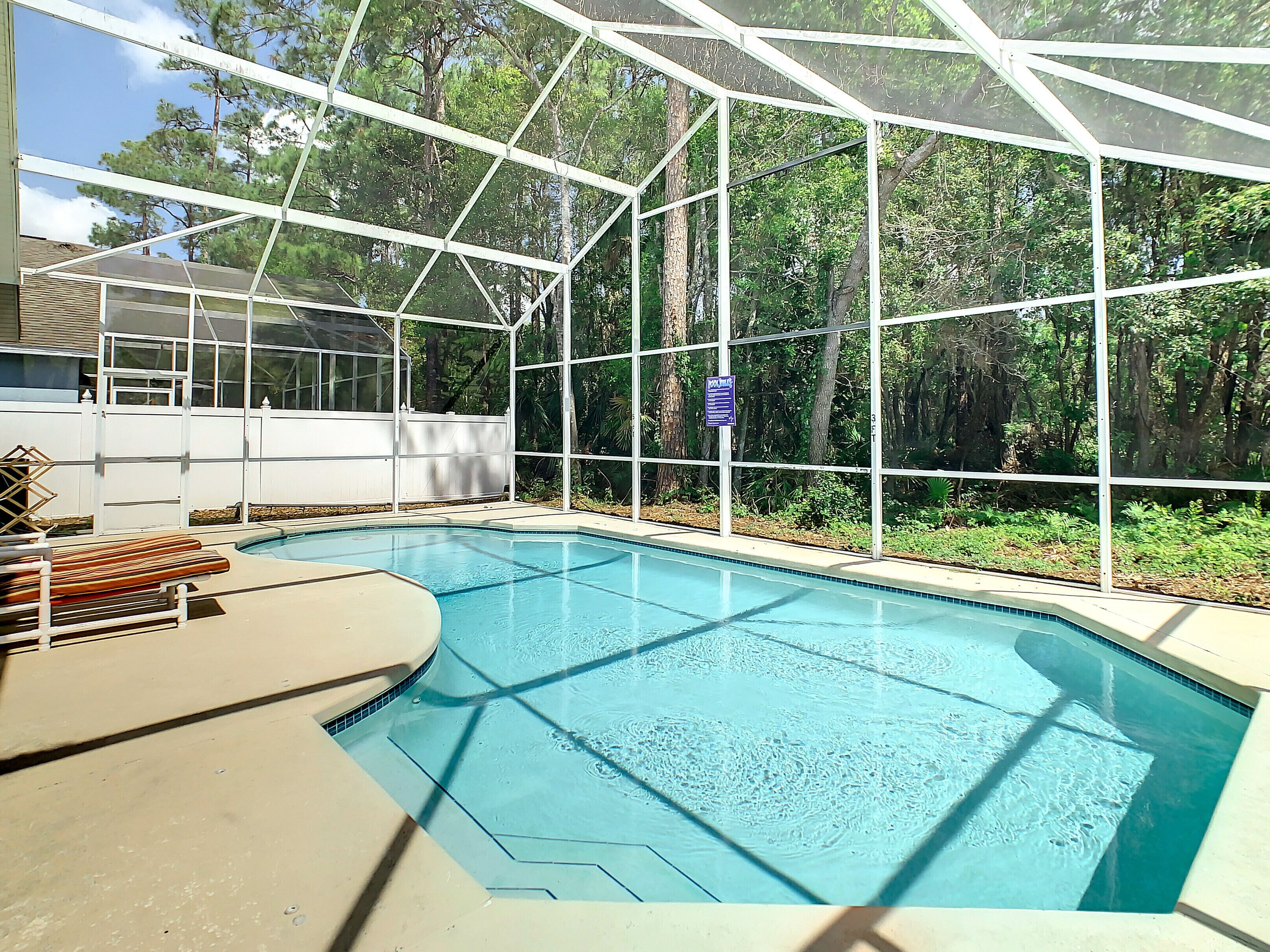 A swimming pool with a glass enclosure, surrounded by a white fence and trees.