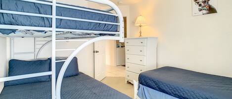 A bunk bed room with a desk and dresser, a lamp, and a framed picture on the wall.
