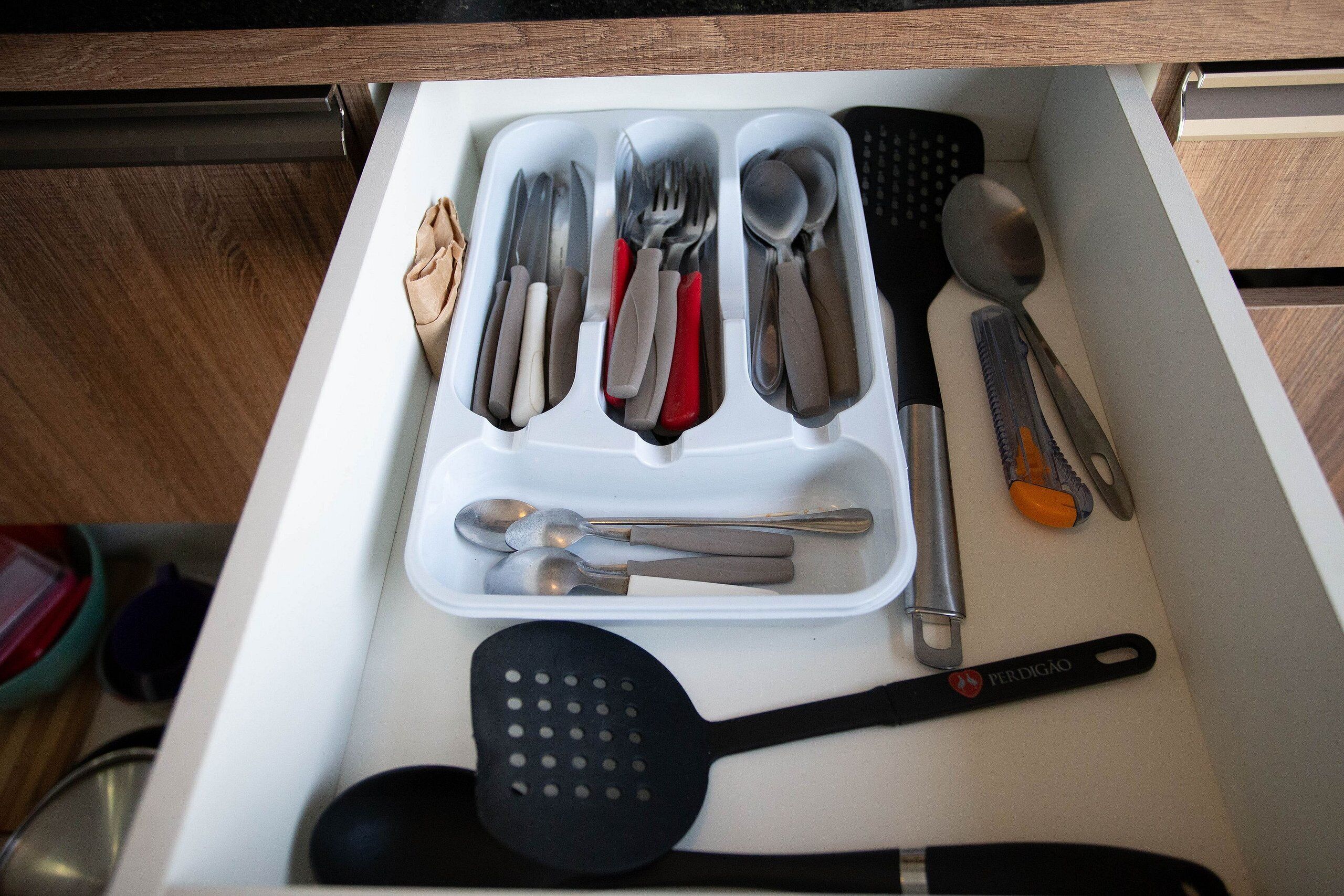 A drawer with kitchen utensils including spoons, forks, knives, and a spatula.