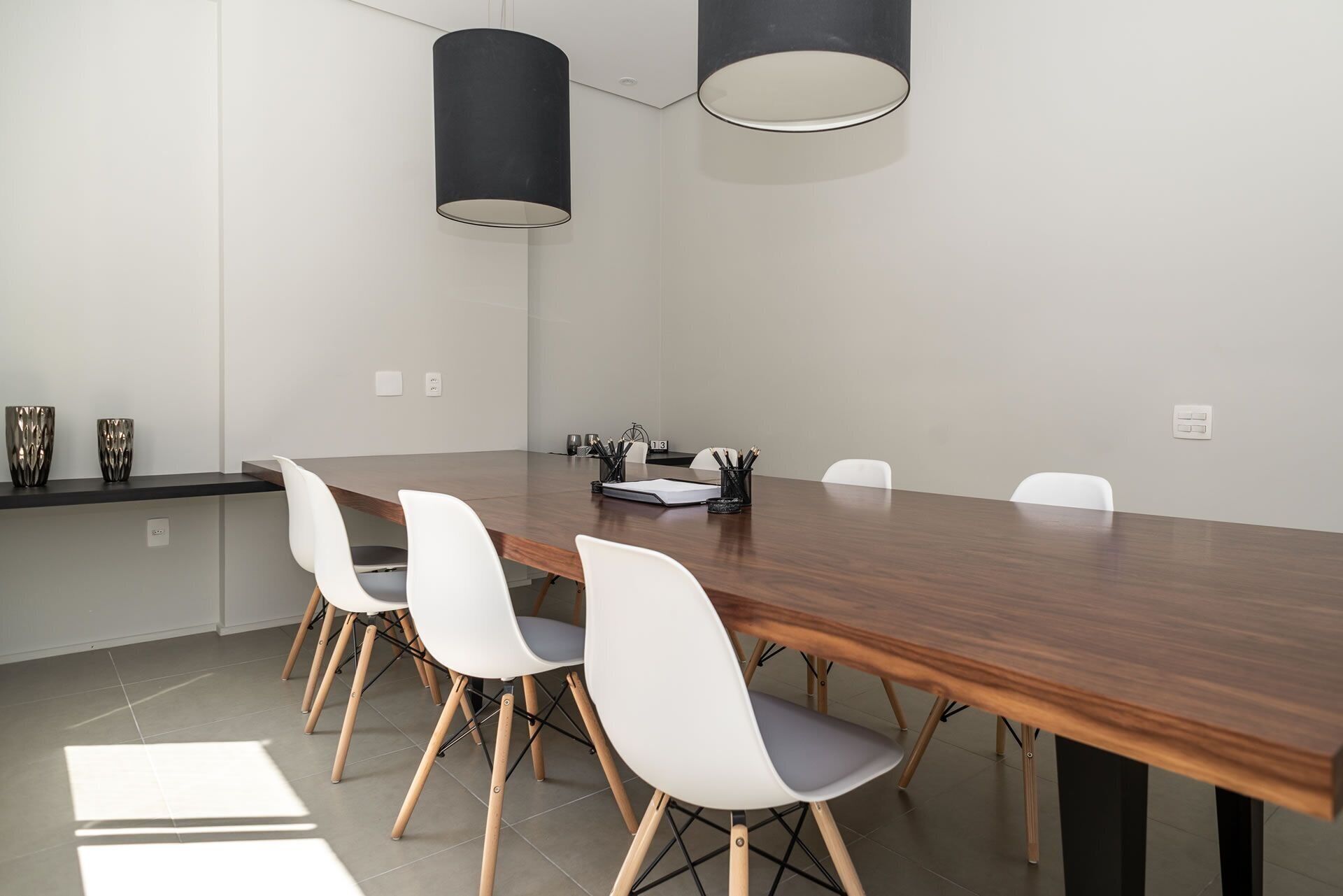 A conference room with a long wooden table, white chairs, and two black pendant lights.