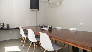 A conference room with a long wooden table, white chairs, and two black pendant lights.