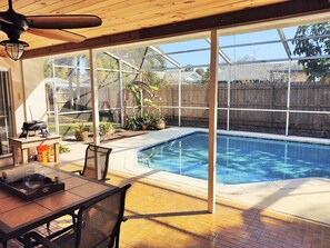 A backyard with a swimming pool, a wooden deck, a table with outdoor seating, and a grill. - Beautiful Beach Style Home by Port Canaveral w/Private Salt Water pool (Merritt Island)