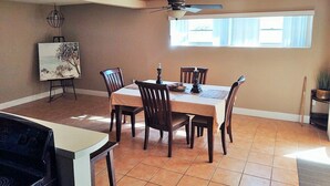 A dining area with a wooden ceiling, a ceiling fan, a table with chairs, a painting on easel, and a window with blinds.