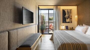 Habitación de hotel con una cama grande, una banca, televisor de pantalla plana montado en la pared y un balcón con mobiliario exterior.
