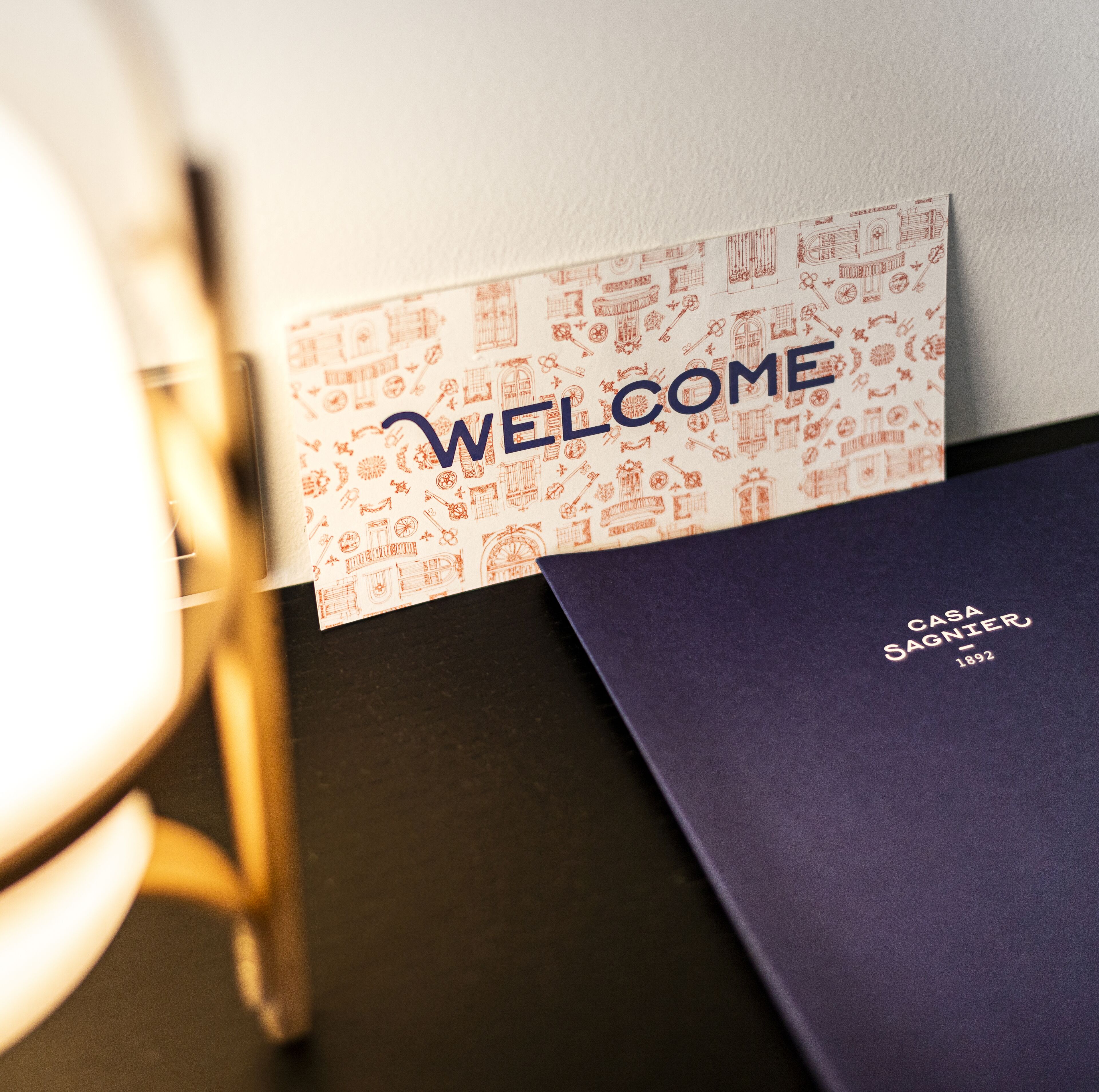 A welcome card with architectural drawings and a dark blue folder with 'CASA SAGNIER 1892' text.