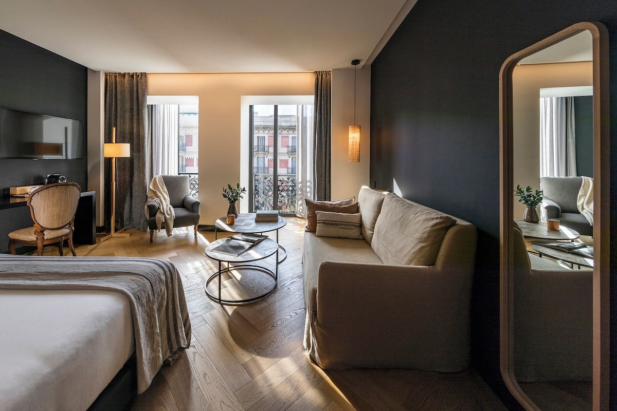 A hotel room with a bed, a sofa, a chair, a desk, and a TV.