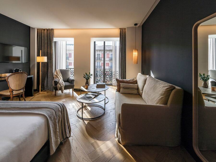 Una habitación de hotel con cama, sofá, sillón, escritorio y televisión.