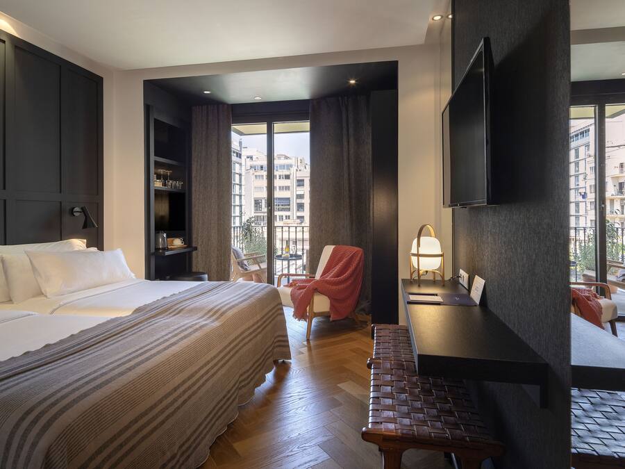 A hotel room with a bed, a desk, a chair, a TV, and a view of the city.