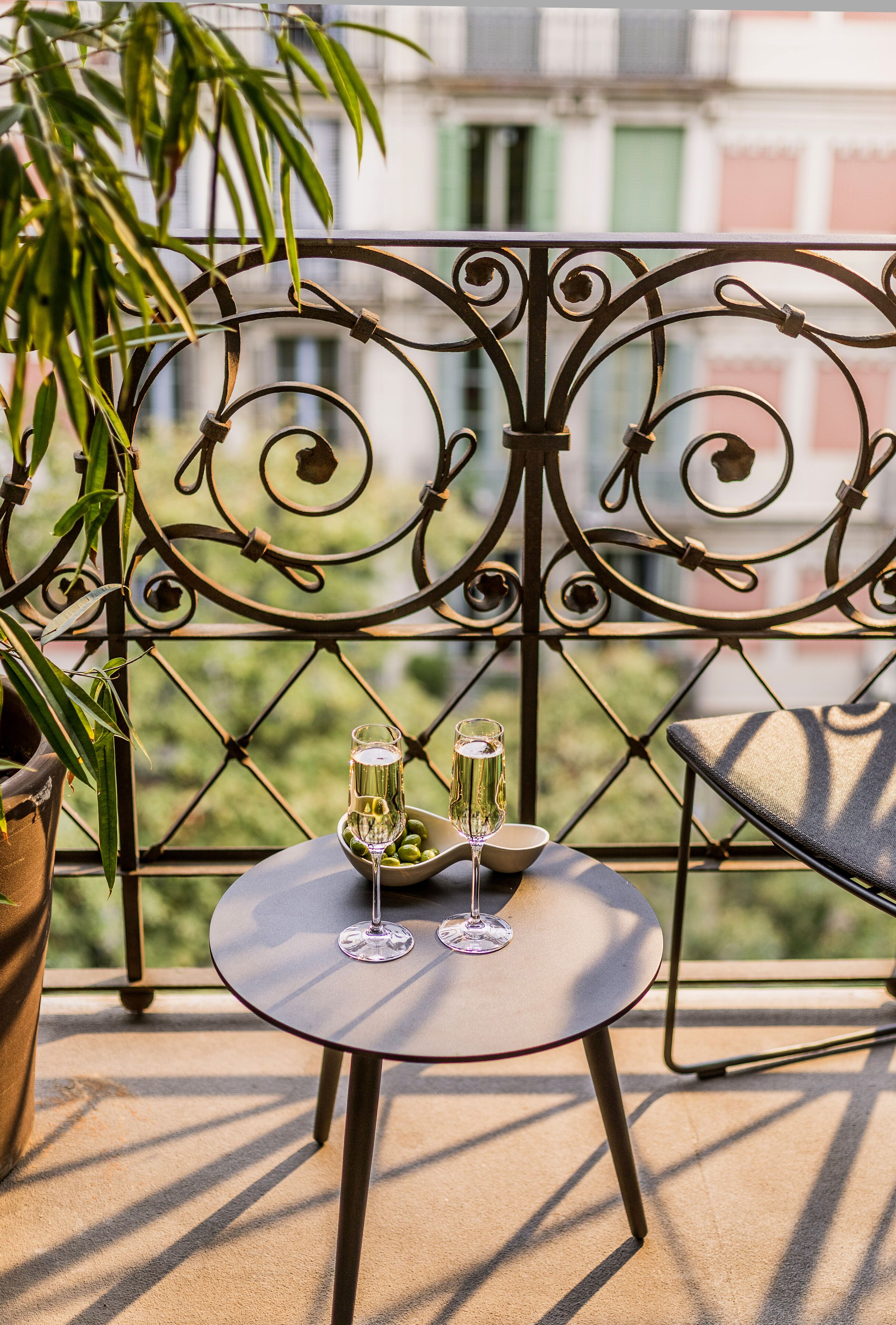 A balcony with a round table, two wine glasses, and a bowl of olives.