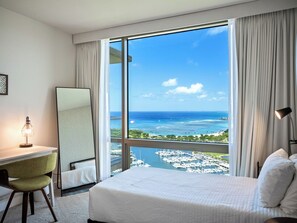 Ein Hotelzimmer mit großem Fenster, einem Bett, einem Schreibtisch und einem Sessel.