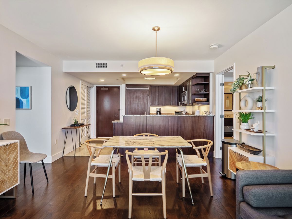 Een moderne eethoek met een houten tafel en stoelen, een keuken op de achtergrond en een boekenplank met decoratieve objecten.