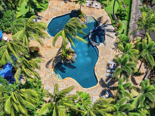 An aerial view of a resort with a central swimming pool surrounded by palm trees and lounge areas.