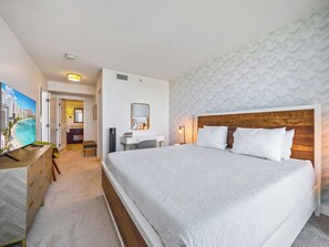 A hotel room with a large bed, a desk with a chair, a television, and a bathroom visible through an open door.