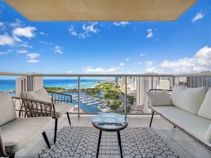 Varanda com vista para o oceano e para a marina, equipada com um sofá, cadeiras e uma mesa.