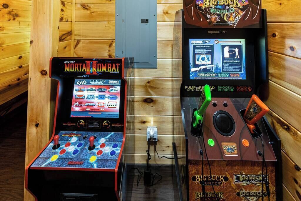 Two arcade machines, one labeled 'Midway Mortal Kombat' and the other 'Big Buck World', in a wooden room.