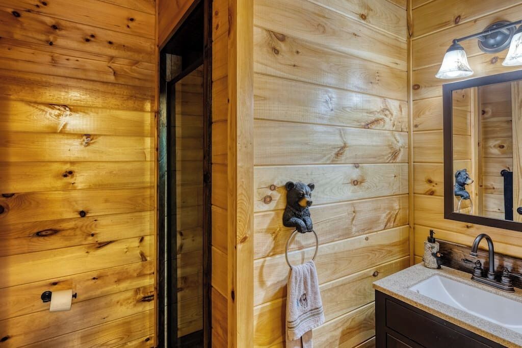 Ein Badezimmer in einer Holzhütte mit Holzwand, einem Waschbecken, einem Spiegel und einem Handtuch an einem Halter.