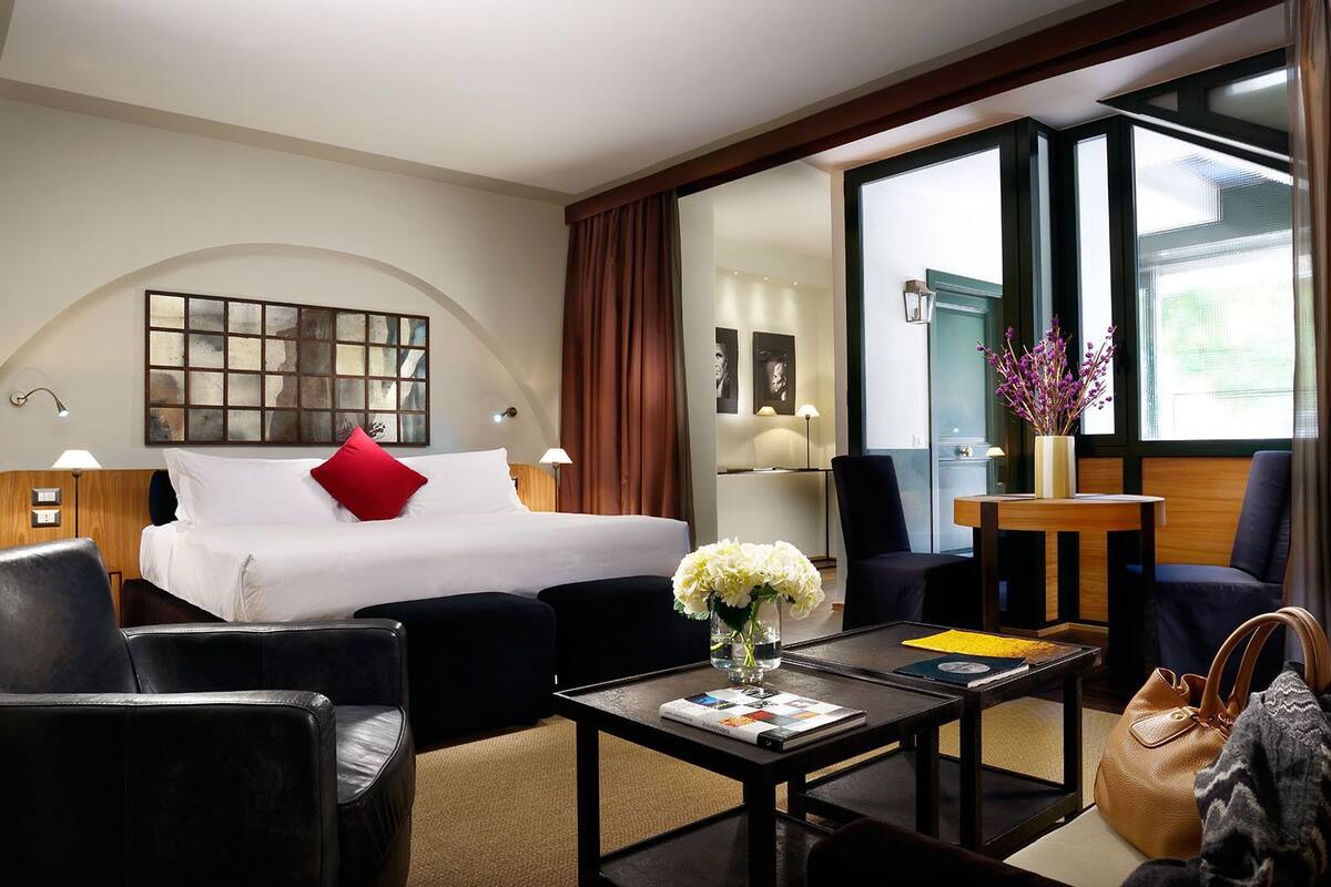 Una habitación de hotel con cama, dos sillas, una mesita de centro y un escritorio con lámpara.