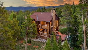 A wooden cabin with large windows, surrounded by trees and a mountainous backdrop. - Mountain Views + Hot Tub + Pet Friendly + Ski Shuttle - Alpenglow Peaks Lodge (Breckenridge)