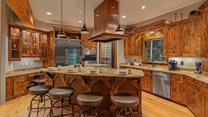 A kitchen with wooden cabinets, stainless steel appliances, and a central island with stools. - Mountain Views + Hot Tub + Pet Friendly + Ski Shuttle - Alpenglow Peaks Lodge (Breckenridge)