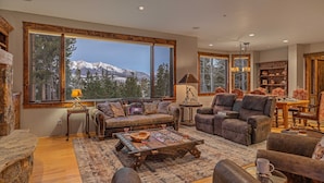 A spacious living room with a large window offering a mountain view, a cozy fireplace, and a dining area with wooden furniture. - Mountain Views + Hot Tub + Pet Friendly + Ski Shuttle - Alpenglow Peaks Lodge (Breckenridge)