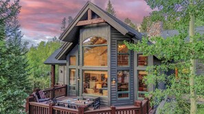 Une grande cabane à plusieurs étages, dotée d’une terrasse et de grandes fenêtres, entourée d’arbres.