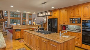 Eine geräumige Küche mit Granit-Arbeitsplatten, Holzschränken, einer zentralen Kochinsel mit Herd und Kühlschrank.