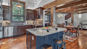 A modern kitchen with a large island, wooden cabinets, and a dining area with a staircase. - Stunning Views | Grand Vista Lodge (Breckenridge)