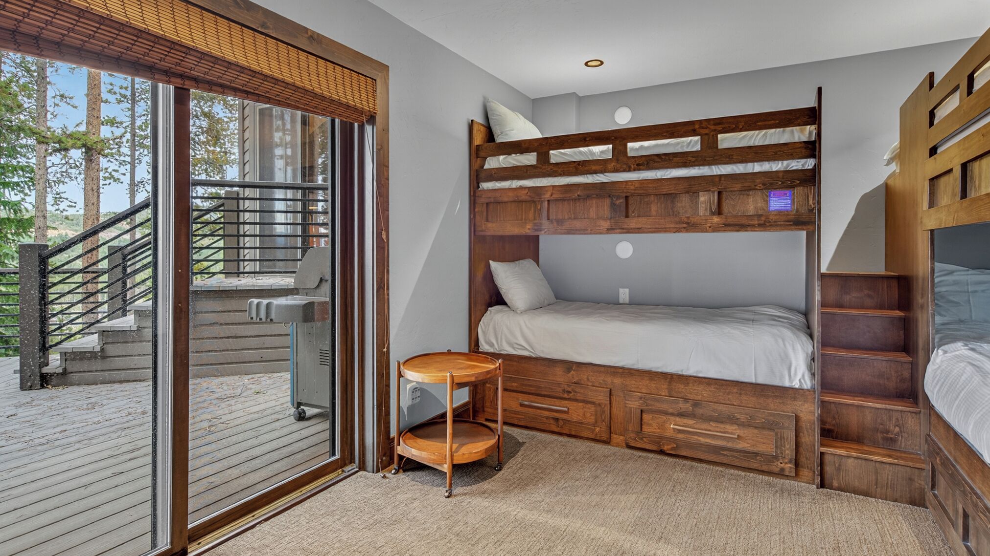 Un dormitorio con una cama litera, una pequeña mesa de madera y un ventanal corredero que da a un área exterior.