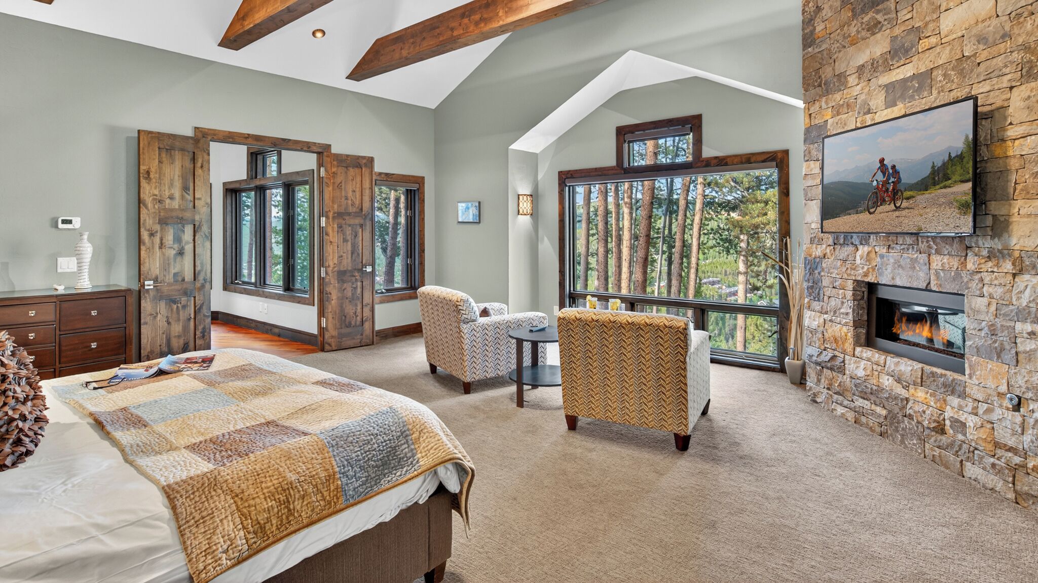 A spacious bedroom with a large bed, a fireplace, and a balcony with a mountain view.