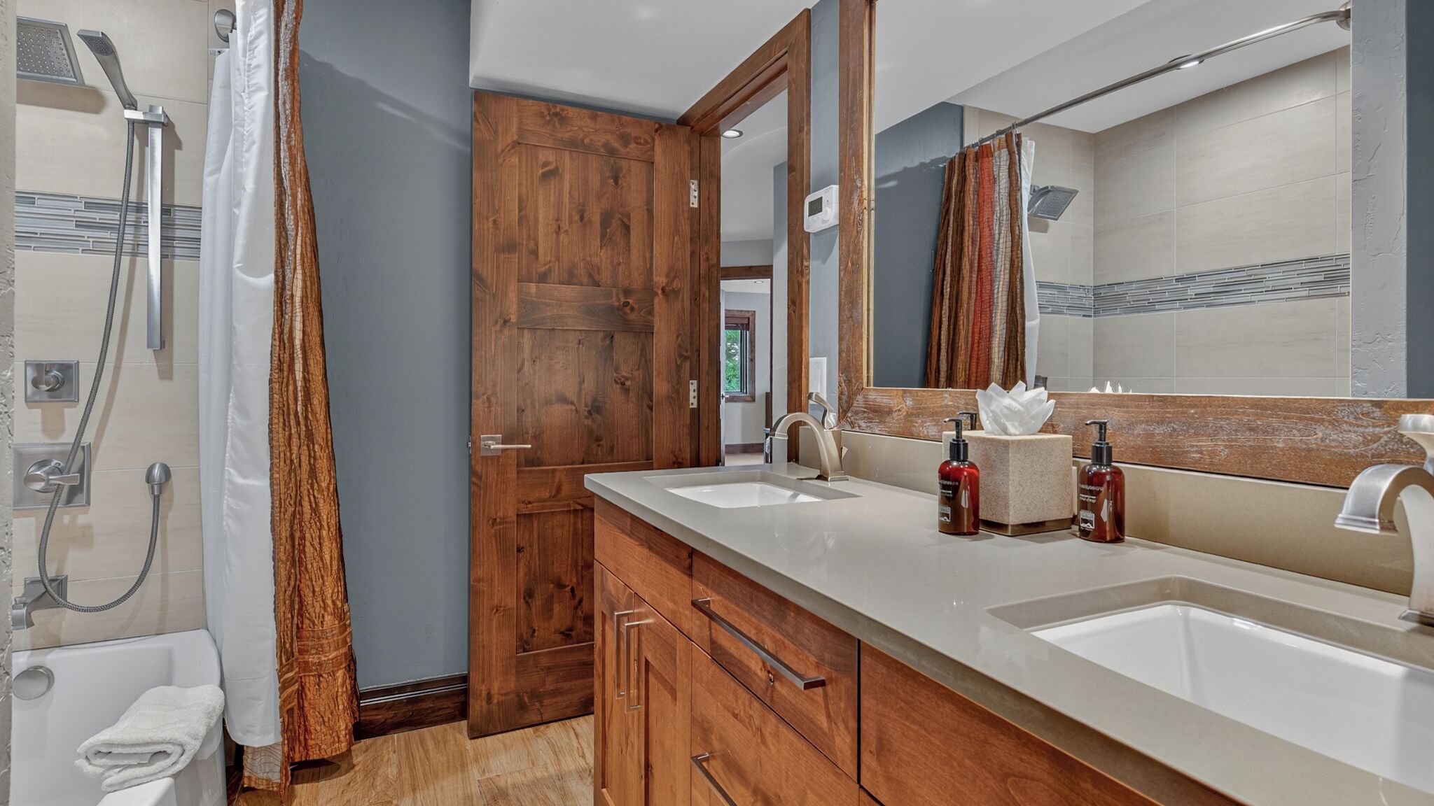 A modern bathroom with a wooden vanity, two sinks, a large mirror, and a shower area.