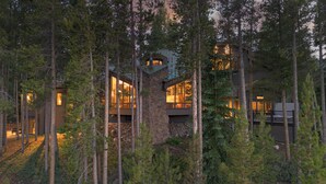 A modern cabin nestled among tall pine trees, featuring large windows and a stone facade. - Stunning Views | Grand Vista Lodge (Breckenridge)