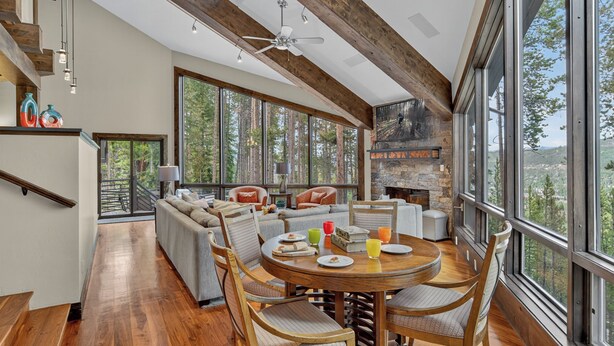A spacious living area with a fireplace, large windows, and a high ceiling with exposed beams. - Stunning Views | Grand Vista Lodge (Breckenridge)
