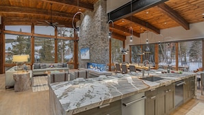 Una cocina amplia con una isla grande, paredes de piedra y ventanas grandes que ofrecen vistas a un paisaje nevado.