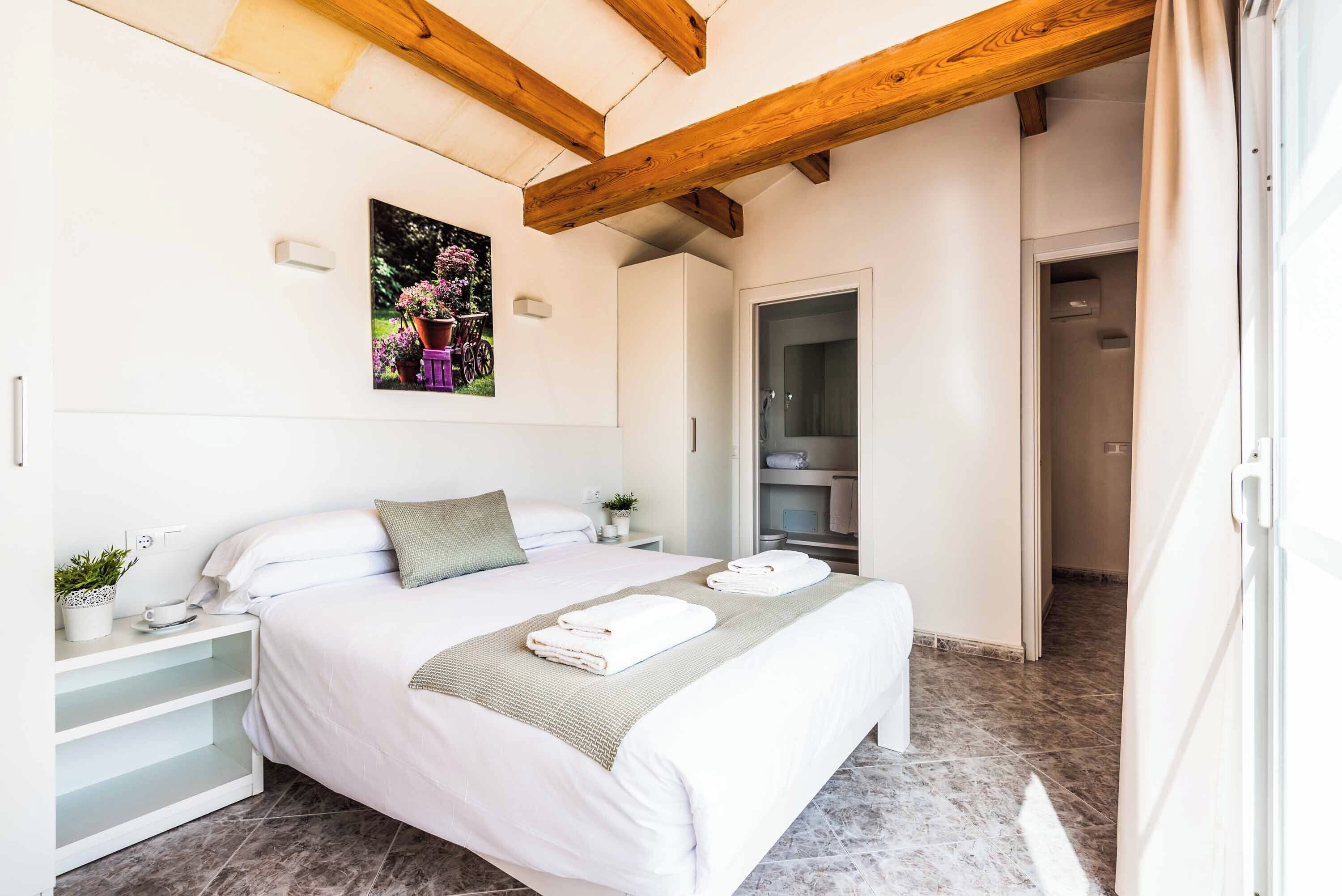 A bedroom with a bed, bedside tables, a nightstand, a painting, a wardrobe, and an open door leading to a bathroom.