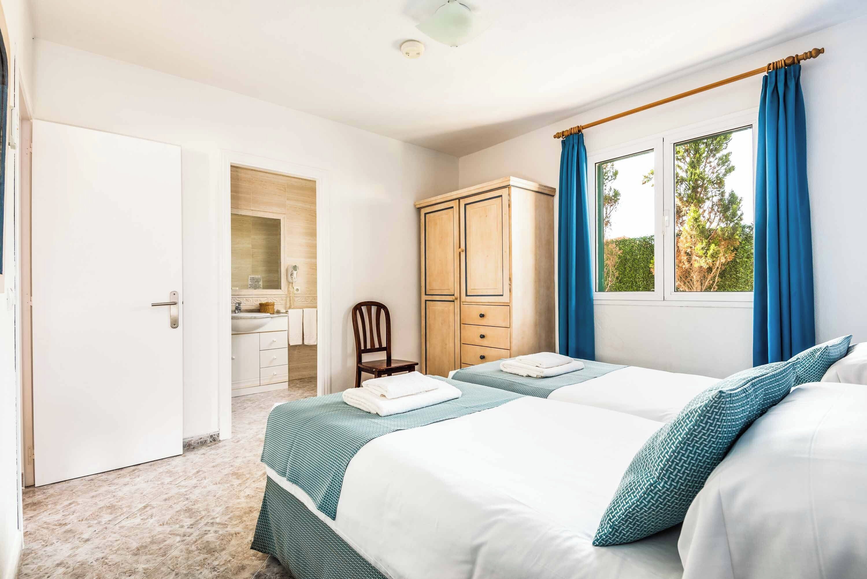 Un dormitorio con dos camas, un armario, baño y ventana con cortinas.