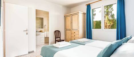 Un dormitorio con dos camas, un armario, baño y ventana con cortinas.