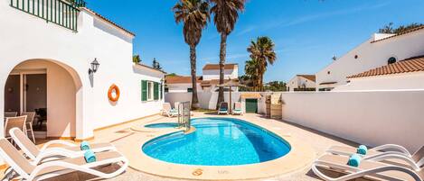A pool area with lounge chairs, palm trees, and a clear blue sky.