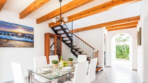A dining area with a glass table, white chairs, a wooden staircase, and a view of the outdoors.