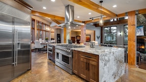 A modern kitchen with a large island, stainless steel appliances, and wooden beams.