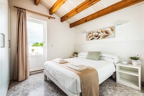 Een slaapkamer met een bed, een nachtkastje, een raam met gordijnen en een schilderij aan de muur.