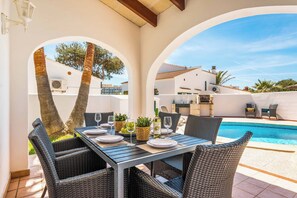 An outdoor dining area with a pool view, wicker furniture, and a table set for two. - Villa Raquel Blanes - Six Bedroom Villa, Sleeps 6 (Los Delfines)
