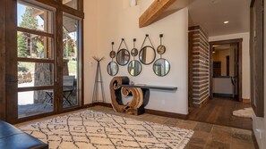 A spacious entryway with a large glass door leading outside, a decorative mirror wall, a wooden console table, and a patterned rug. - Designer Home + Ski in/Ski out + Hot Tub + Pet-Friendly | Epic Retreat (Breckenridge)