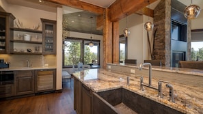A modern kitchen with a large island, wooden beams, and a stone fireplace. - Designer Home + Ski in/Ski out + Hot Tub - Epic Retreat (Breckenridge)