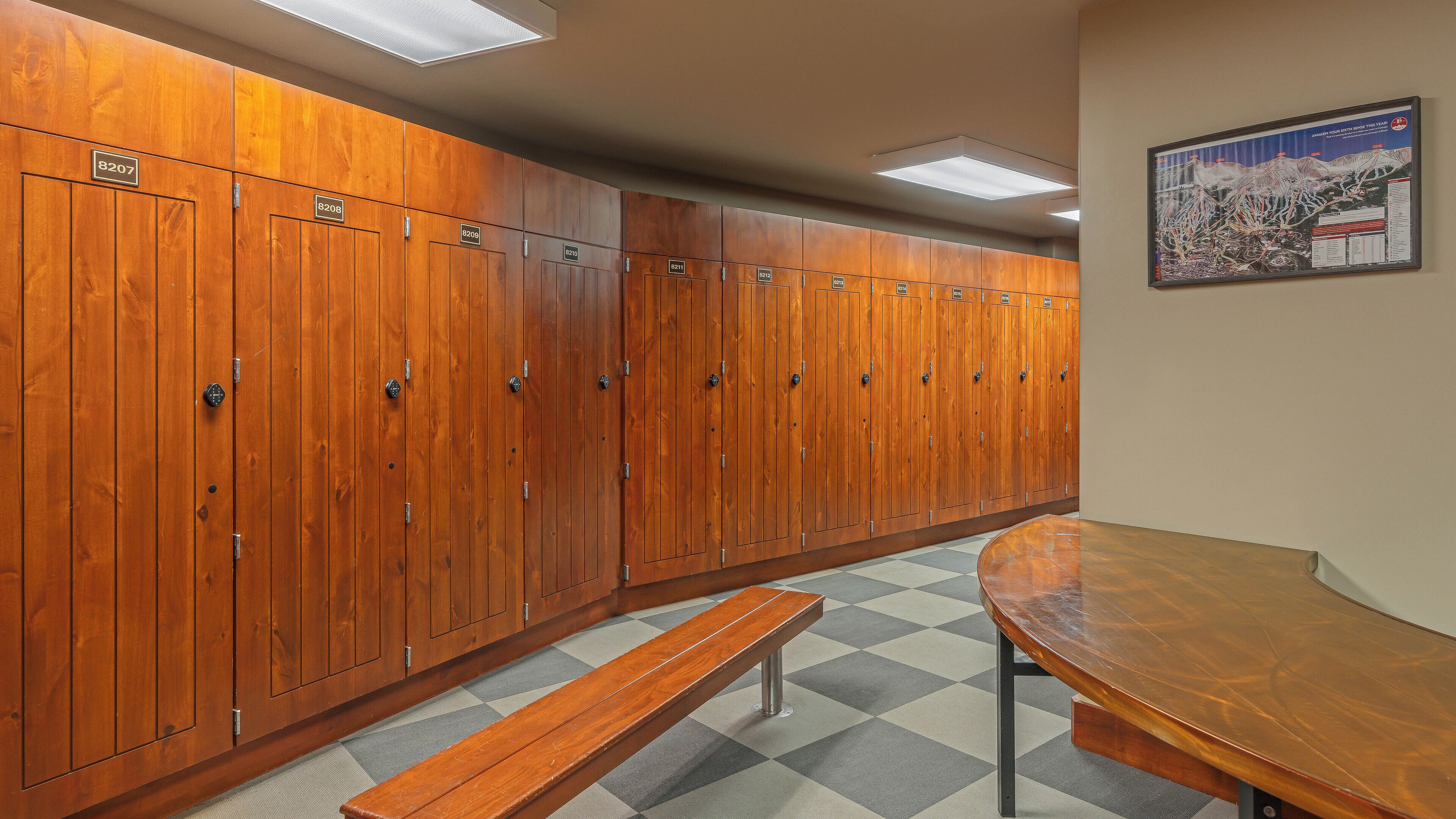 A row of wooden lockers with numbers, a bench, and a table in a locker room.