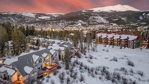 A snow-covered mountain town with a prominent lodge featuring a red exterior and multiple balconies. - Luxury w/Mountain Views + Ski-in/Ski-out - Pines 75 Townhome (Breckenridge)