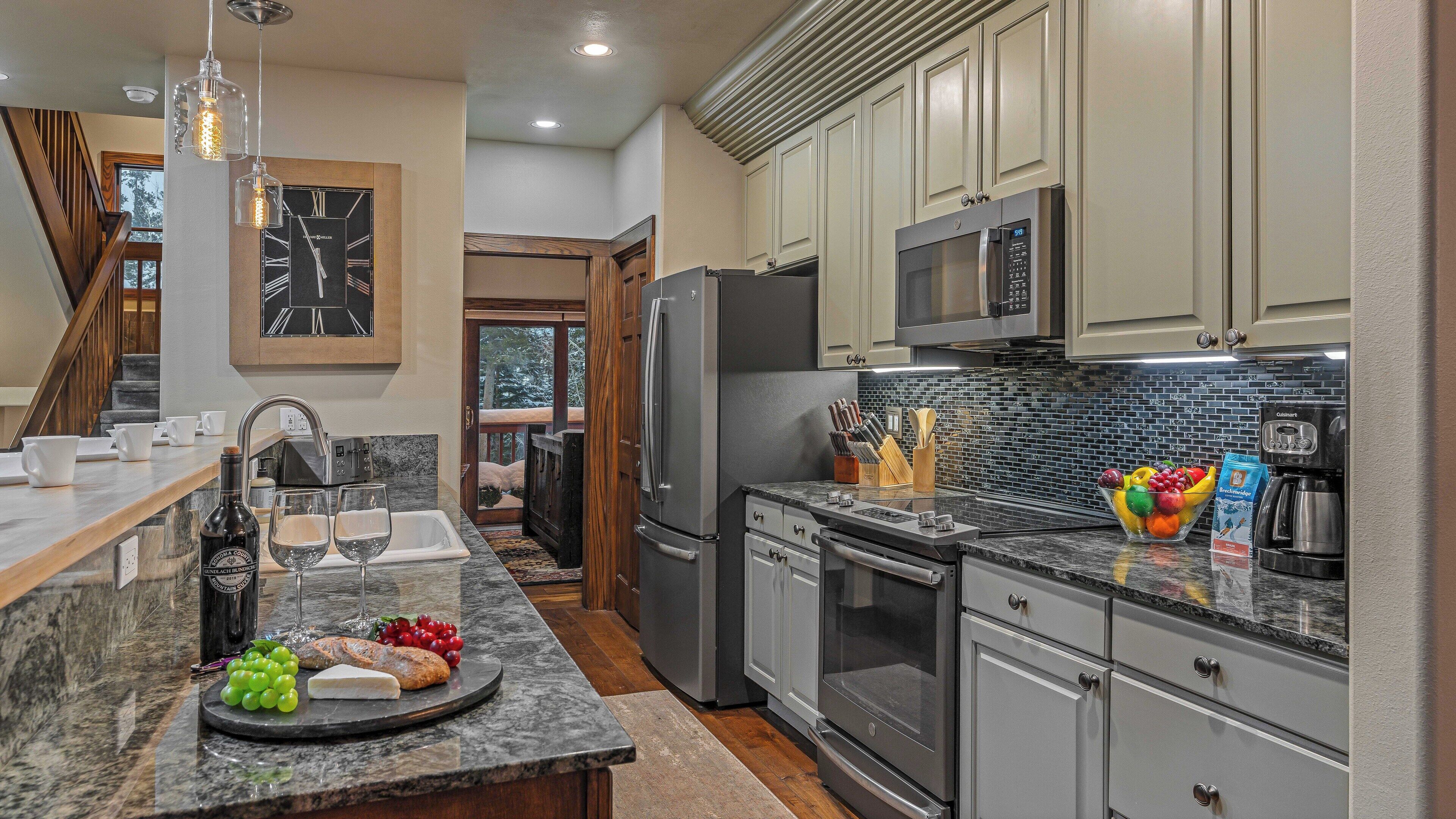 A modern kitchen with stainless steel appliances, a marble countertop, and a view to the outside.