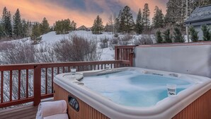 A hot tub on a wooden deck with a view of a snowy landscape and trees.